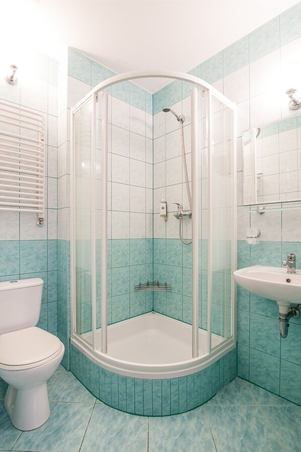 Un baño con ducha compartimentada por vidrio, inodoro y lavamanos.