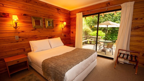 A wooden room with a bed, a nightstand, a bench, and a table with chairs. - Cabañas Playa Linda (Villarrica)