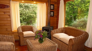 A cozy room with wicker furniture, a fireplace, and large windows overlooking greenery. - Cabañas Playa Linda (Villarrica)