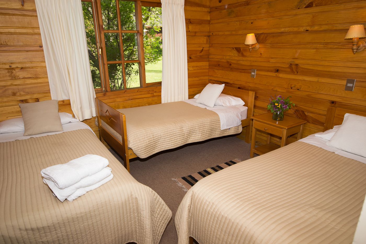 A cabin-style room with two beds, a small table, and a window with curtains.