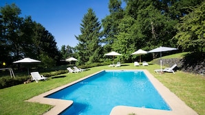 A rectangular swimming pool with a tiled edge, surrounded by a grassy area with white lounge chairs and umbrellas. - Cabañas Playa Linda (Villarrica)