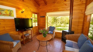 A cozy wooden cabin interior with wicker furniture, a television, and a fireplace. - Cabañas Playa Linda (Villarrica)