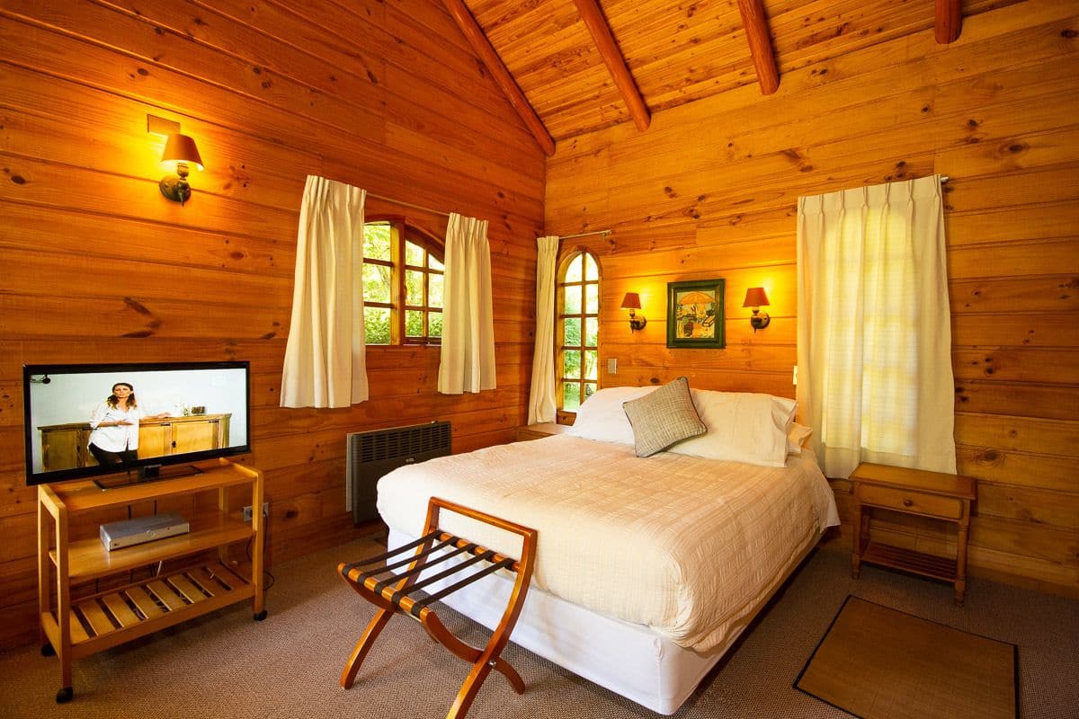 Une chambre confortable, aménagée dans un chalet en bois, avec un lit, un téléviseur posé sur un meuble en bois et une fenêtre avec des rideaux.