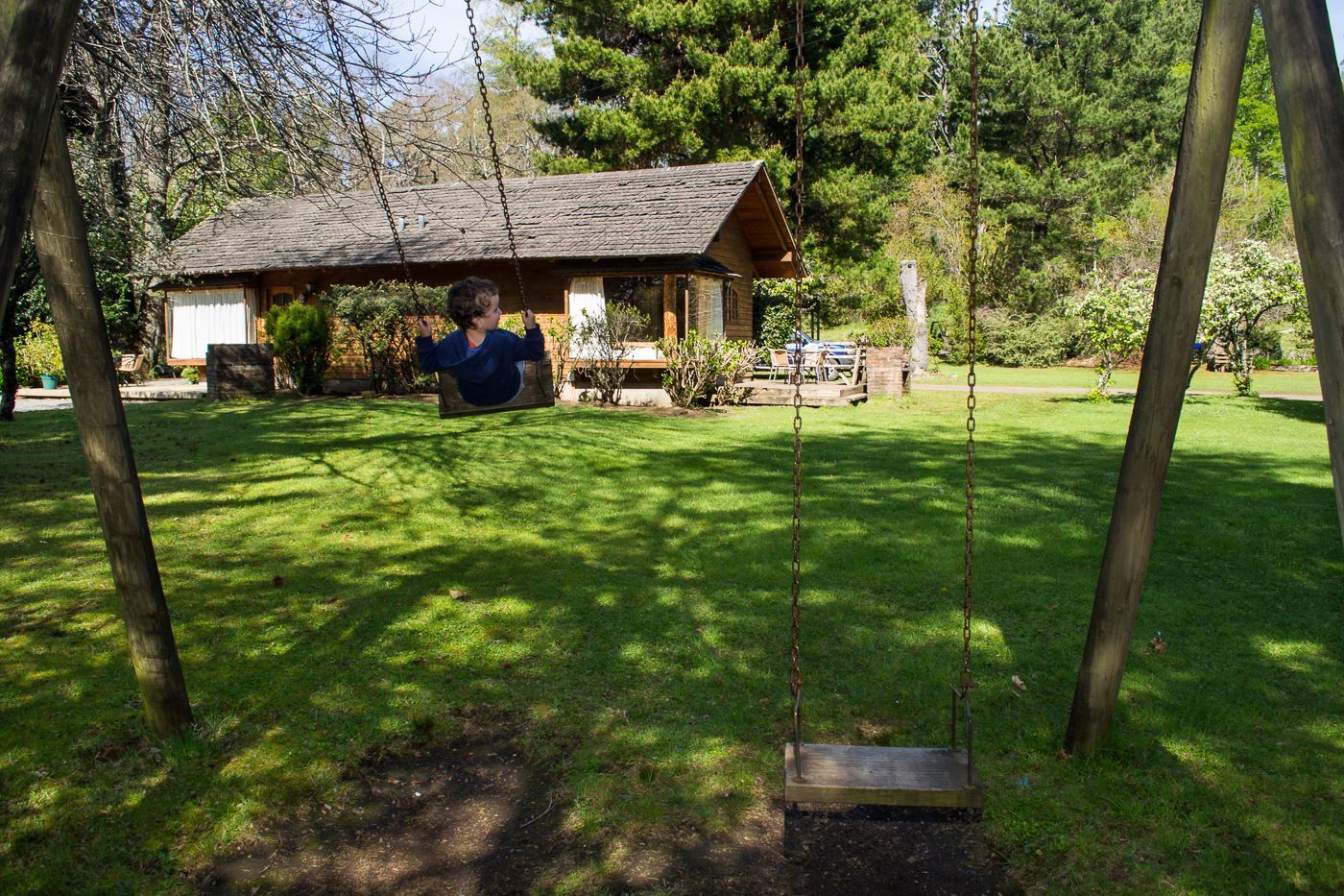 A wooden swing set in a grassy area with a rustic cabin in the background.