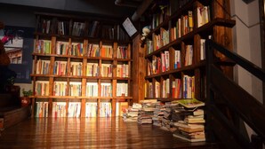 Una biblioteca con estanterías de madera llenas de libros, suelo de madera y una pila de libros en el suelo.