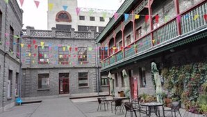 Un patio con un edificio de piedra, mobiliario exterior y banderas coloridas.