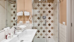Un baño moderno con ducha de vidrio, un espejo grande y un lavamanos blanco con artículos de tocador.