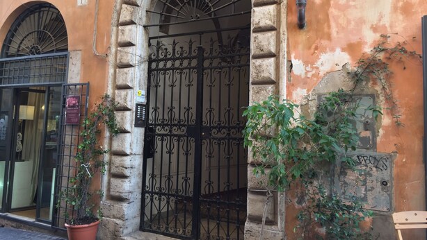 Un edificio con una entrada en arco, una puerta metálica y plantas en macetas.