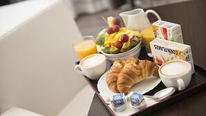 Bandeja de desayuno con cruasanes, café, jugo y un tazón de fruta.