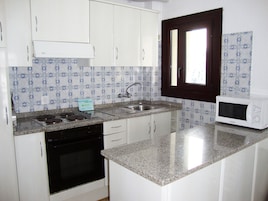 Una cocina con gabinetes blancos, una estufa negra, un fregadero y un microondas.