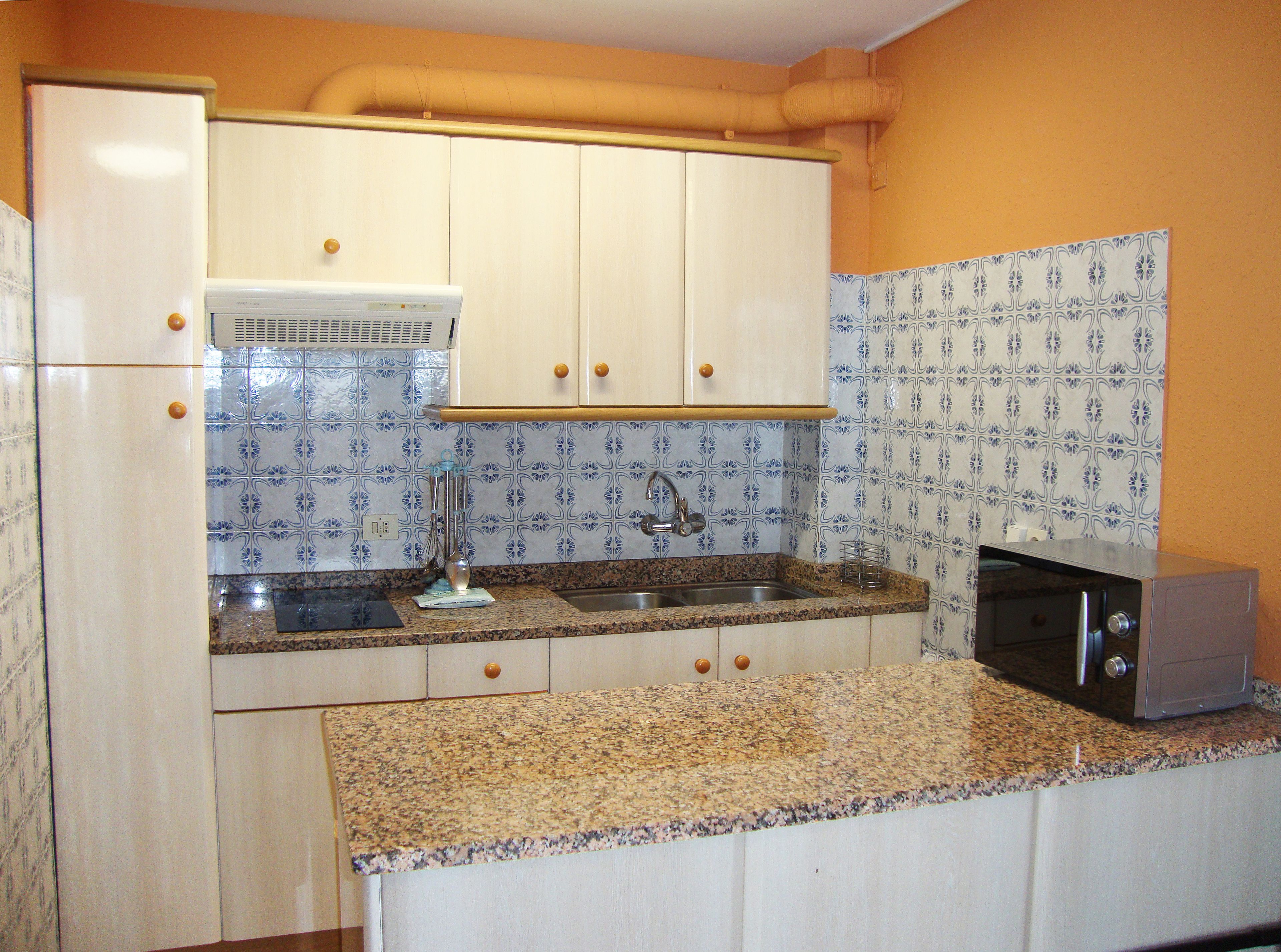 Una cocina con armarios blancos, encimera de granito, fregadero y microondas.