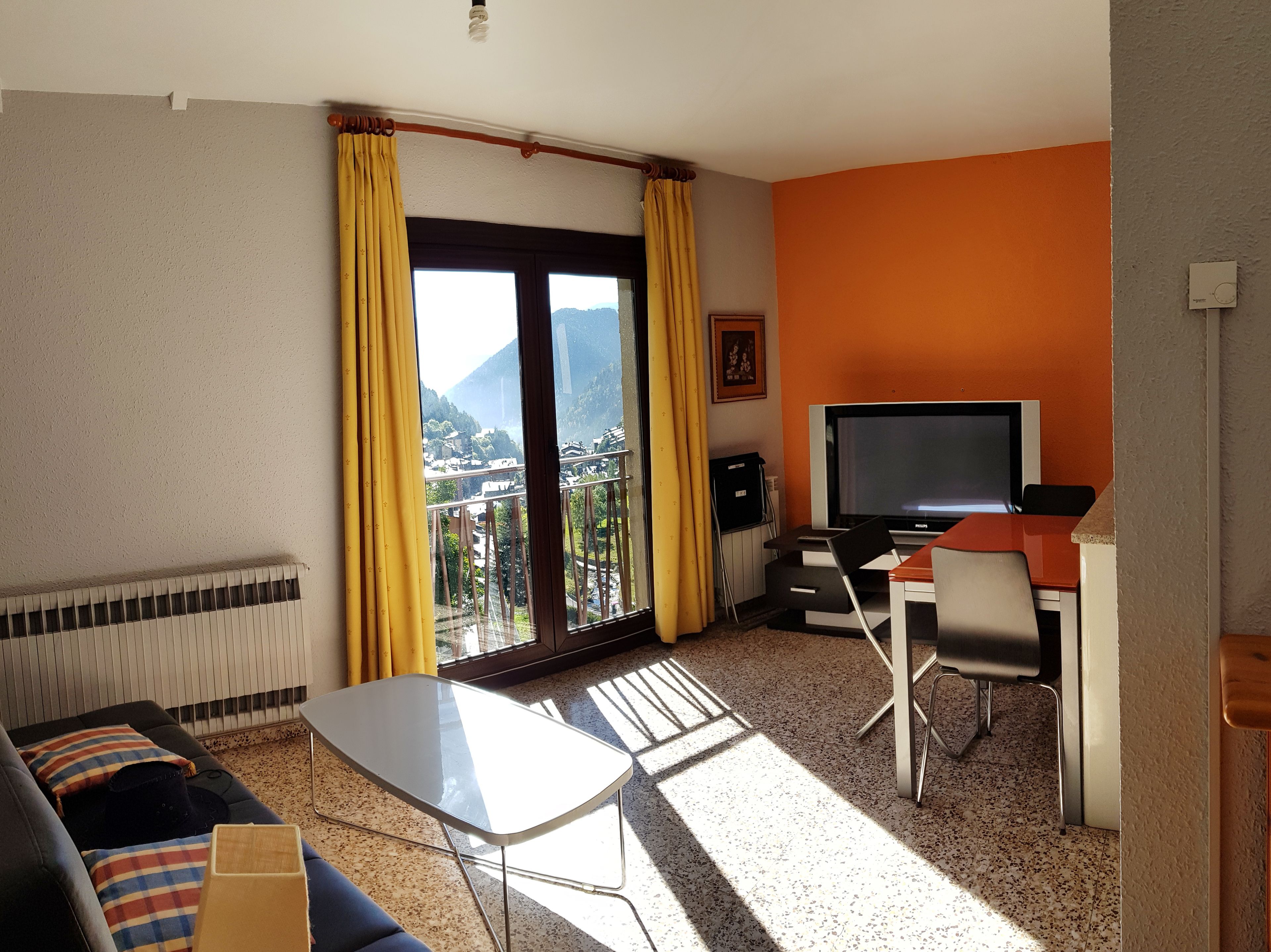 Una habitación de hotel con balcón, televisión, sofá, mesa y silla.