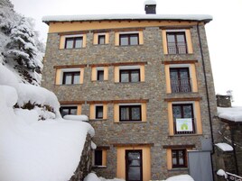 Un edificio de piedra de varios pisos con múltiples ventanas y balcones, rodeado de árboles cubiertos de nieve.