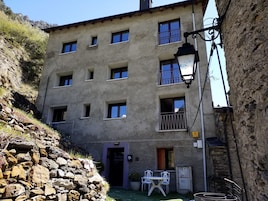 Un edificio de varios pisos con fachada de piedra, varias ventanas y un pequeño espacio al aire libre con una mesa y sillas.