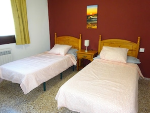 Une chambre double avec deux lits simples, une table de chevet avec une lampe, un tableau au mur et une fenêtre avec des rideaux.