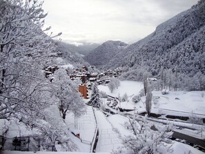 A snow-covered village with traditional buildings, a river, and a mountainous backdrop. - Apartamentos Arinsal 3000 (Arinsal)