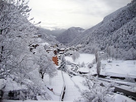 Un pueblo cubierto de nieve con edificios tradicionales, un río y montañas al fondo.