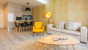 A modern living room with a sofa, a yellow chair, a dining table with chairs, a coffee table with candles, and a kitchen area with cabinets and a pendant light. - Innapartments - Passos Manuel (Porto)