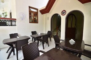A dining area with a table and chairs, a fan, and a window. - OYO 9741 Triple Beach Guest House (Benaulim)