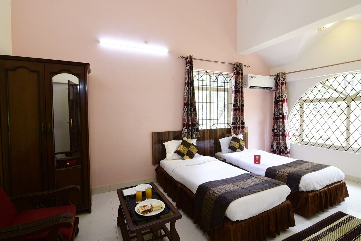 A hotel room with two beds, a wooden wardrobe, a desk with a tray of food, and a window with curtains.