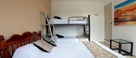 A hotel room with a bunk bed, a wooden headboard, a small table, and a painting on the wall.