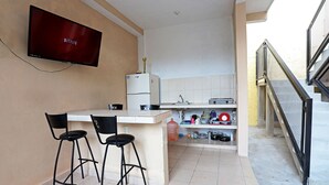 Cocina compacta con una televisión montada en la pared, un refrigerador, un lavamanos y una pequeña zona de bar con dos taburetes.