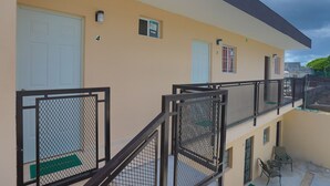 Un edificio de varios pisos con balcones, puertas numeradas y un felpudo verde en la entrada.