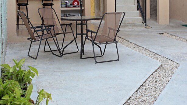 Un patio al aire libre con una mesa, sillas, un paraguas blanco y una escalera que sube a un nivel superior.