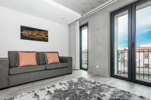 A modern living room with a grey sofa, a cityscape painting, and a large window with a view of buildings. - Innapartments - São Gonçalinho (Aveiro)