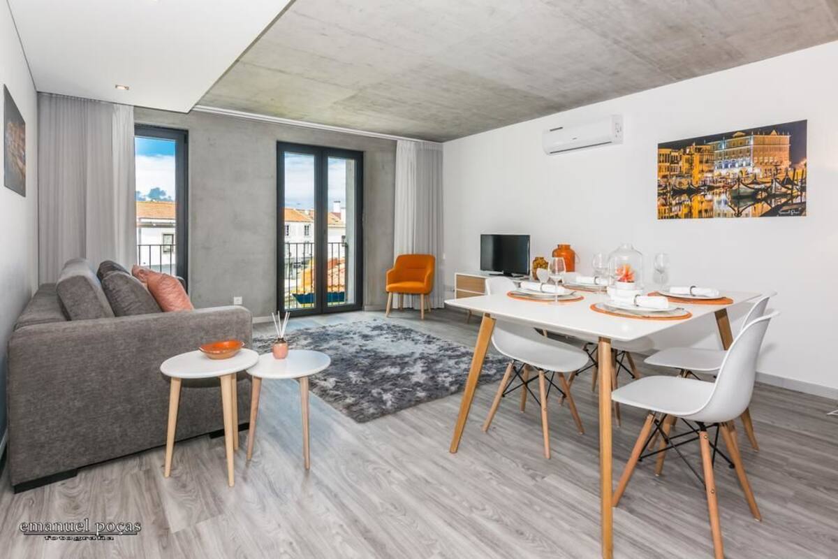 A modern living room with a grey sofa, a dining table with white chairs, and a TV.