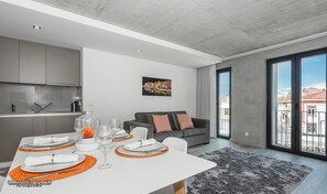 A modern living room with a dining area, grey sofa, and a cityscape view through large windows. - Innapartments - São Gonçalinho (Aveiro)