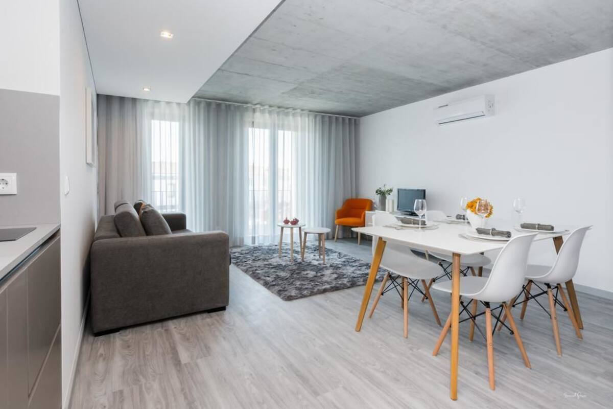 A modern living room with a grey sofa, a dining table with chairs, and a small orange chair.