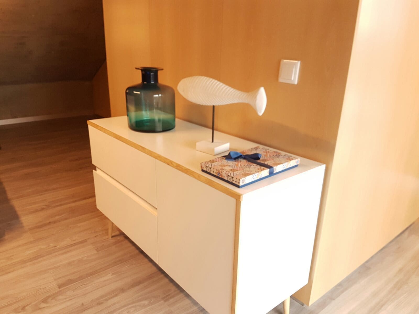 A white desk with a glass bottle, a white lamp, and a notebook with a blue ribbon.