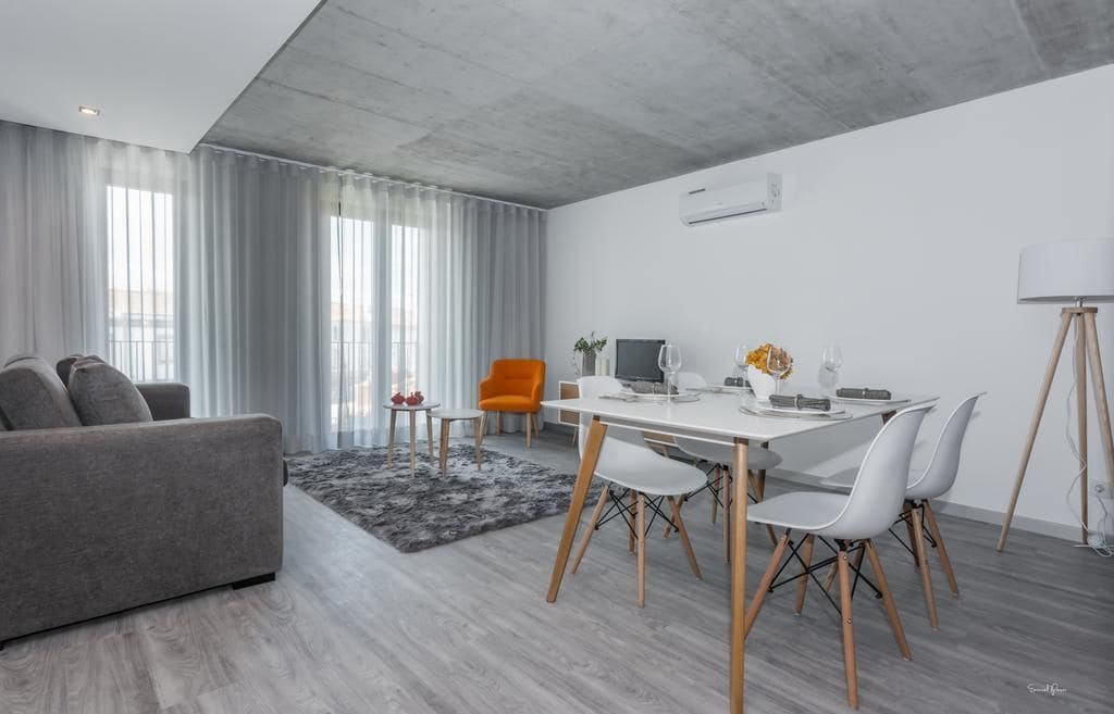 Una sala de estar moderna con un sofá gris, una mesa de comedor con sillas blancas y una alfombra gris.