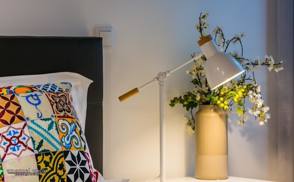 A neatly made bed with a colorful, patterned blanket, a bedside lamp, and a vase with flowers.