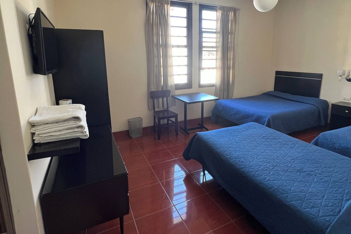 Habitación de hotel con dos camas, un escritorio, una silla, un televisor y una ventana con cortinas.