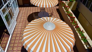 A rooftop terrace with two large striped umbrellas, a patterned floor, and a flower planter along the wall. - Hotel Tito (Arequipa)