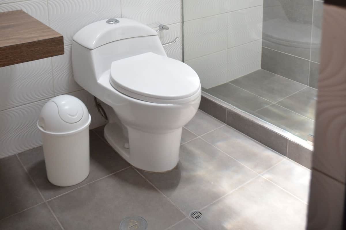Un baño moderno con inodoro, un cubo de basura y una ducha con mampara de vidrio.