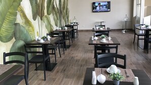 A restaurant with tables set for dining, a large mural of leaves on the wall, and a TV screen displaying a news program. - Hotel Tito (Arequipa)
