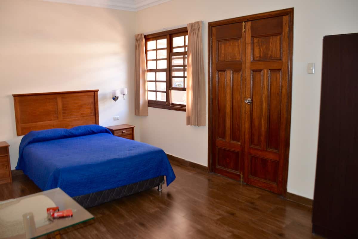 Un dormitorio con una cama de madera, una mesita de noche, un aparador y una ventana con cortinas.