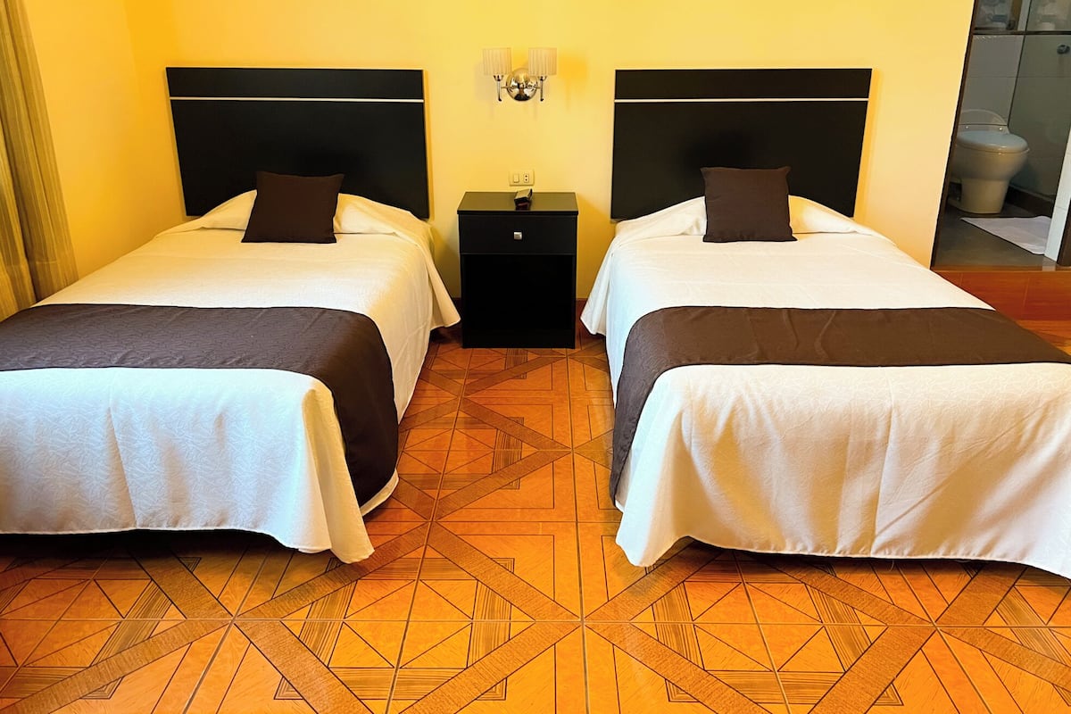 Habitación de hotel con dos camas, una mesita de noche y una lámpara de pared.
