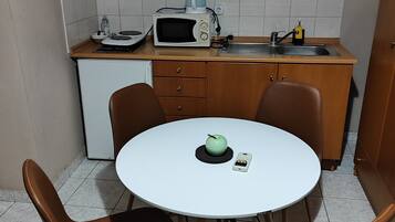 Une petite cuisine équipée d’un four à micro-ondes, d’une bouilloire et d’un évier. On y trouve une table ronde avec des chaises, et une pomme verte posée dessus.