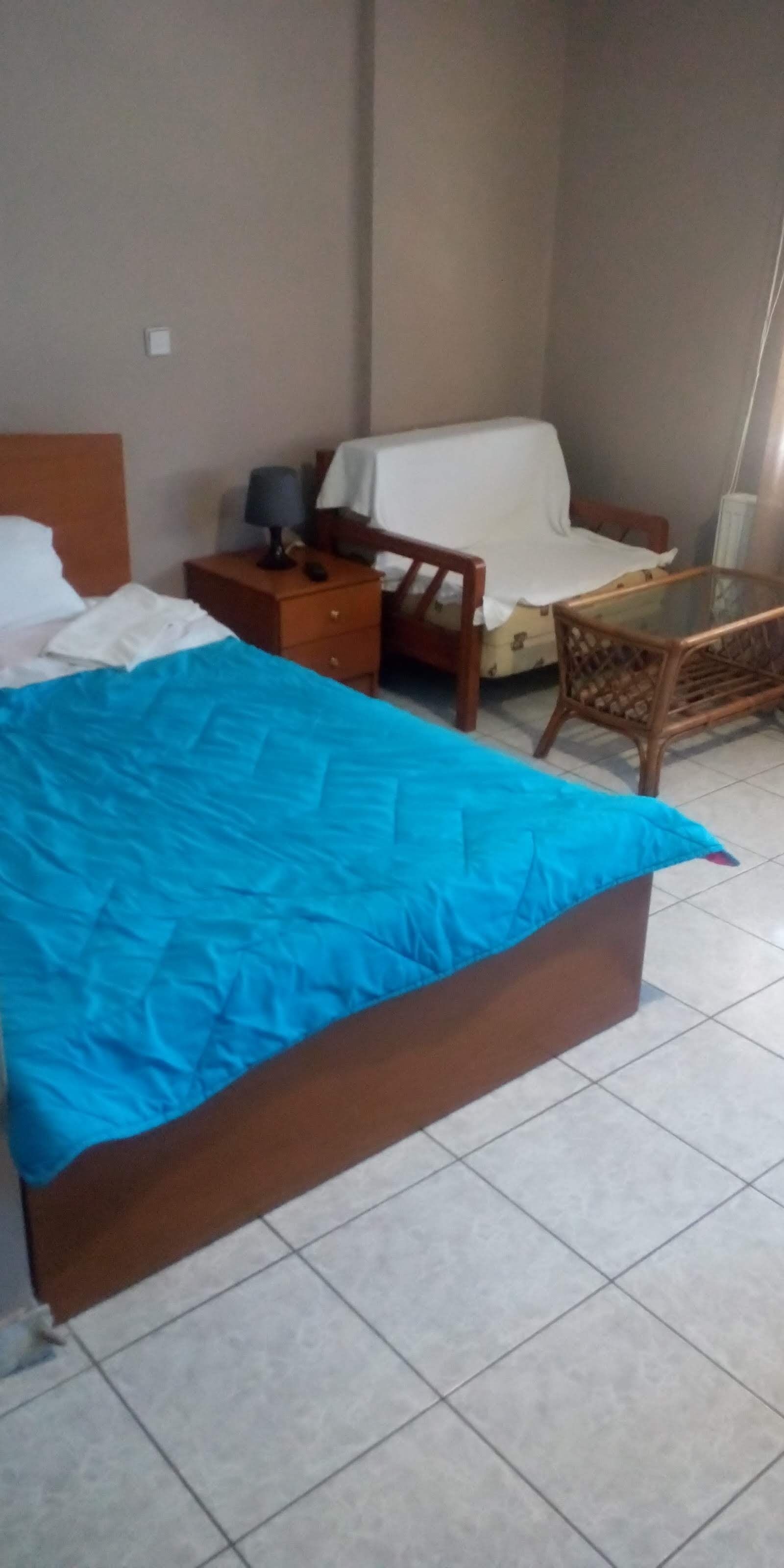 Une chambre d’hôtel avec un lit, une table de chevet en bois, une petite table et un canapé recouvert d’une housse.