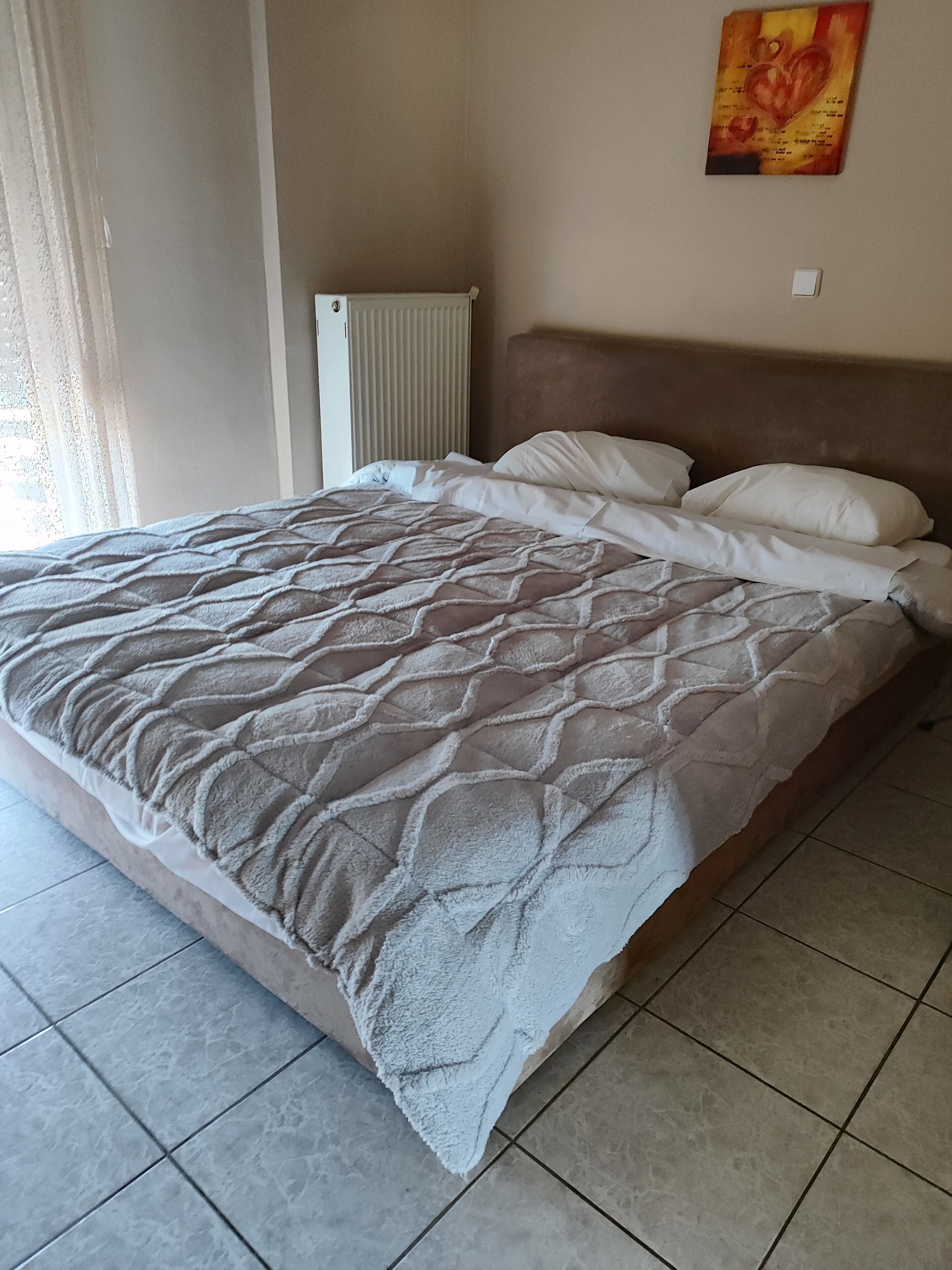 A bed with a quilted cover, a radiator, and a wall with a framed picture.