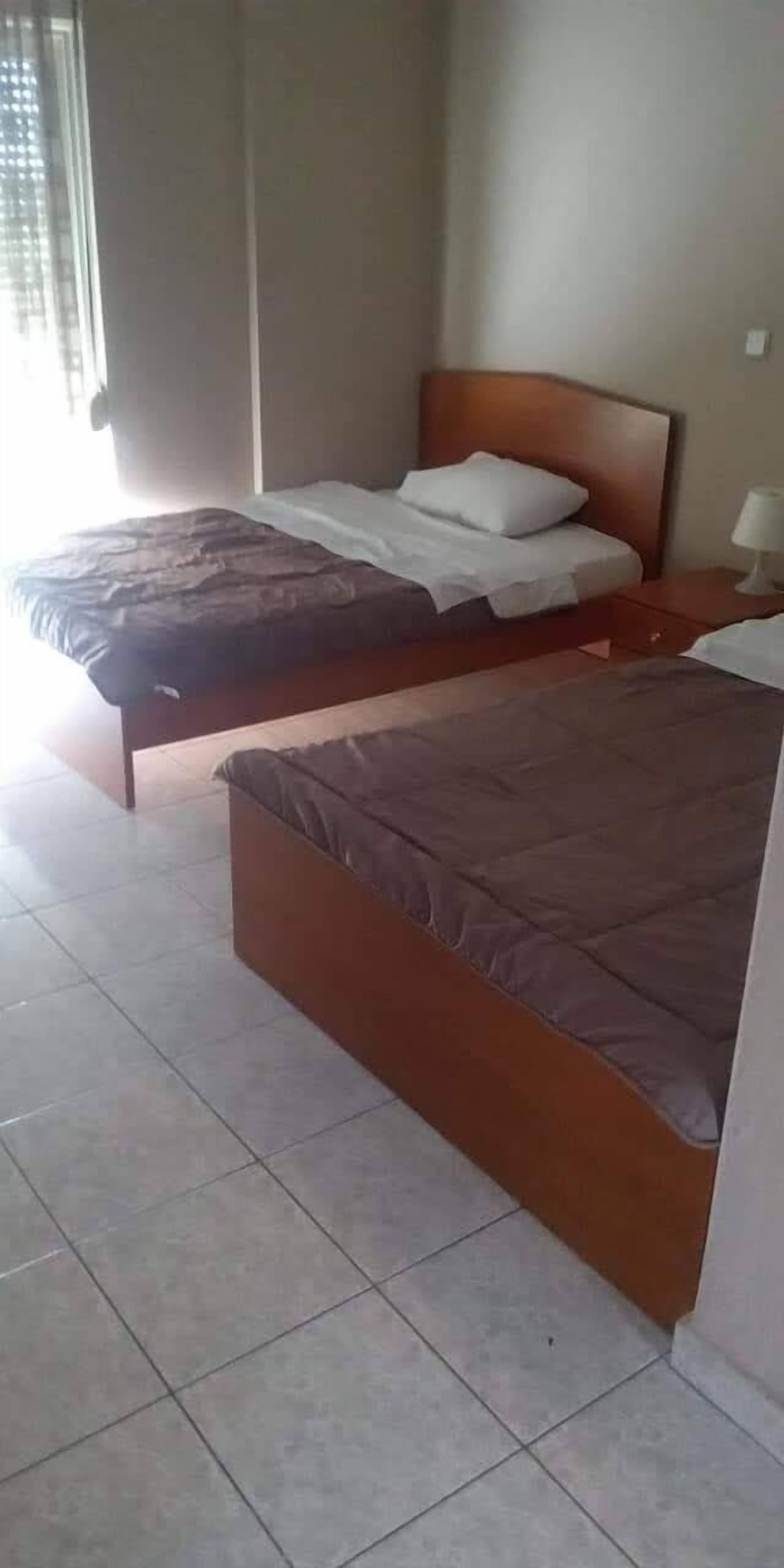 Habitación de hotel con dos camas, un cabecero de madera, una mesita de noche con lámpara y una ventana con persianas.