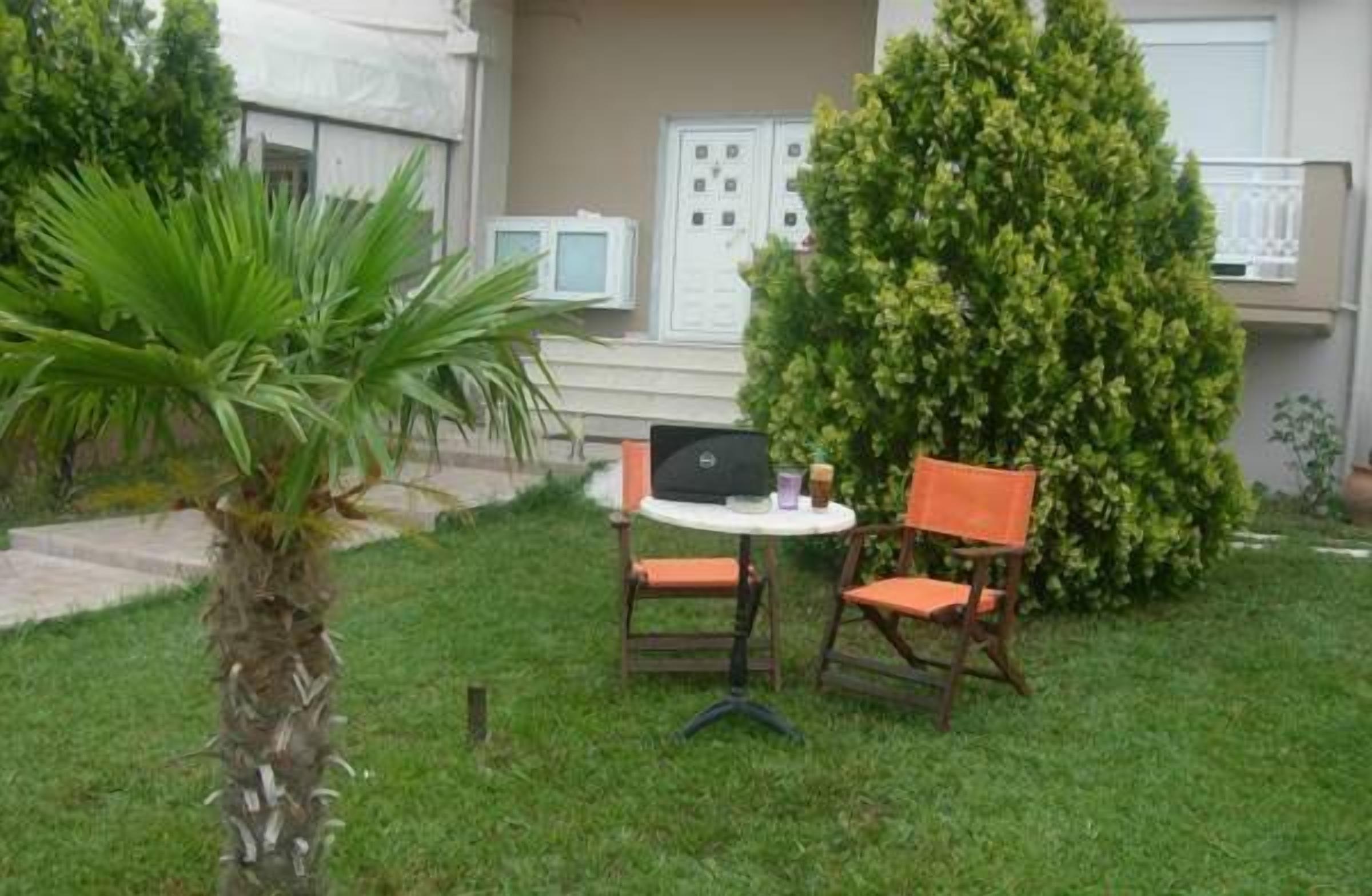 Un pequeño espacio al aire libre con una mesa y dos sillas, rodeado de follaje y una palmera.