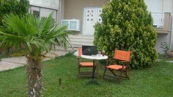 Un pequeño espacio al aire libre con una mesa y dos sillas, rodeado de follaje y una palmera.