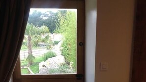 A room with a wooden door, a small white table, and a view of a garden through a window. - Le Colombier de la Graverie (Senots)