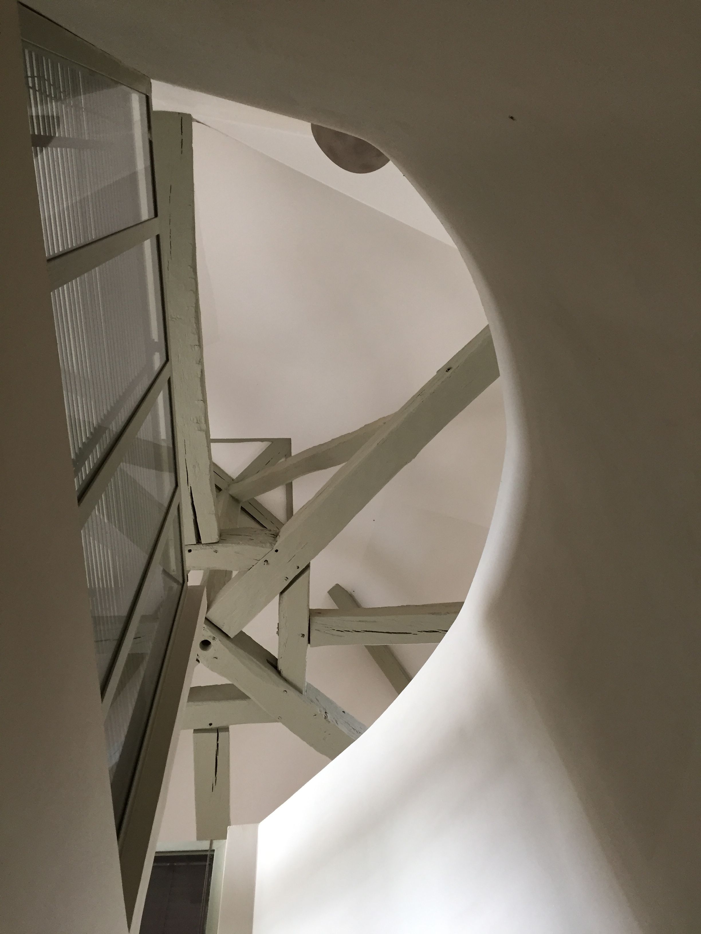 A spiral staircase with a circular opening, wooden beams, and a window with blinds.