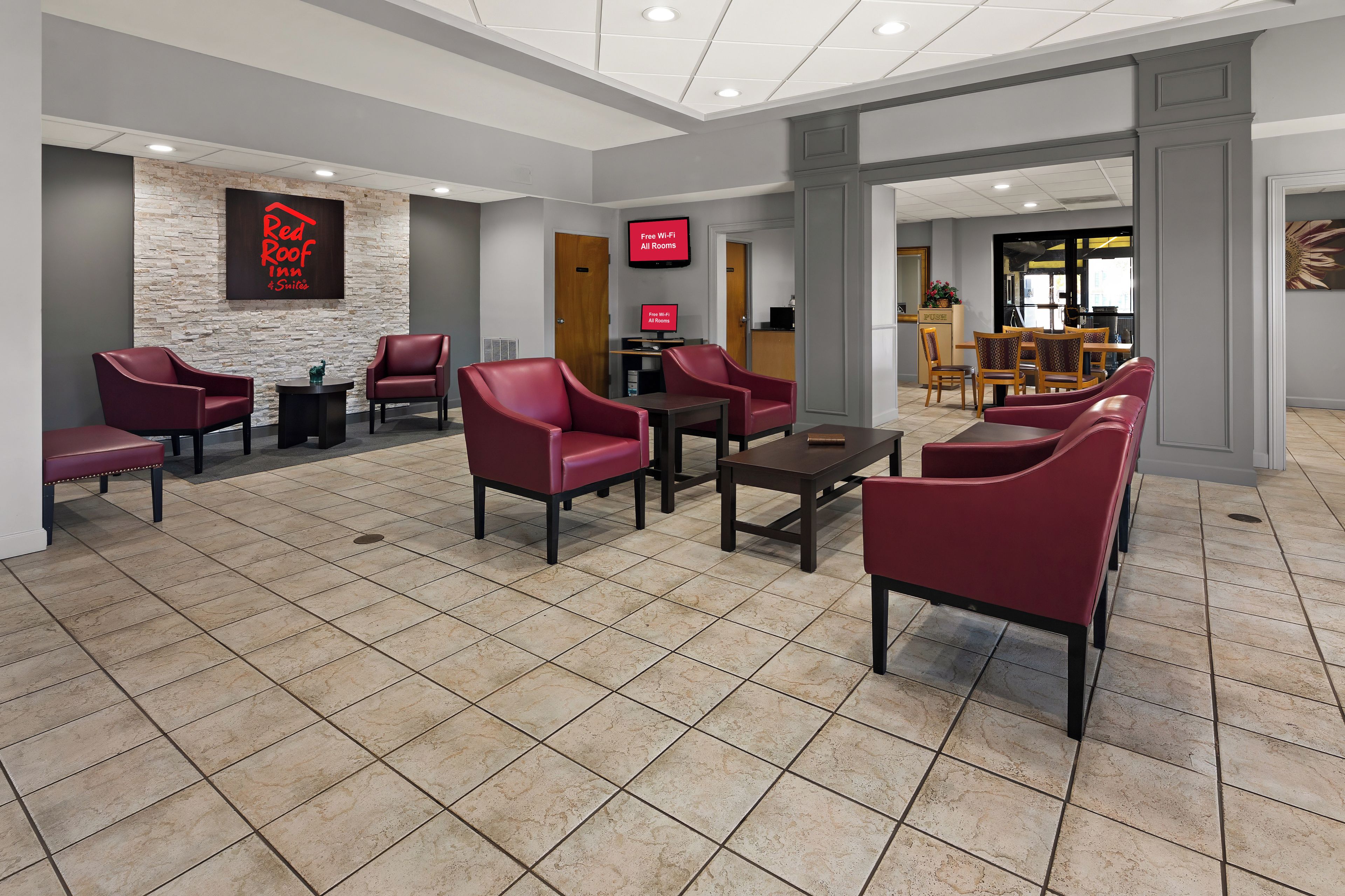 A hotel lobby with red leather chairs, a stone accent wall, a digital screen, and a reception desk.